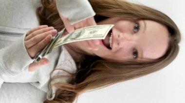 Mutlu genç kız farklı yönlere 100 dolarlık banknotlar saçıyor yavaş çekim videosu beyaz arka plan spor ceketli zengin bir adamın parayı çöpe atması üzerine. Geleceği düşünmüyorum.