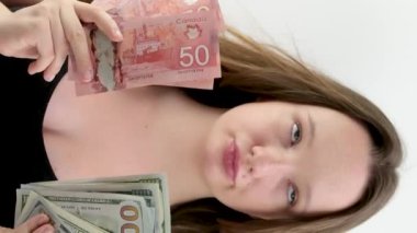 Kanada doları ve Amerikan doları arasında seçim yapmak kız elinde beş paket Kanada doları ve dudak büken büyük 100 dolarlık banknotlarla çok para seçer. yolculuk hediyesi