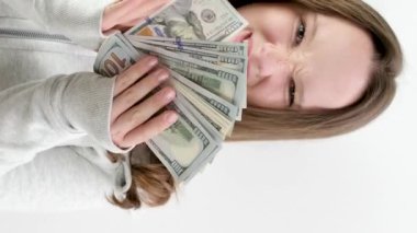 Genç kız, büyük miktarda para gösteriyor. Ailesinden para çalan bir tomar para gösteriyor. Stüdyoda beyaz arka planda 100 dolar. Faturalar ve genç bir kadın.