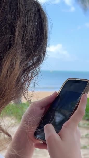 女の子はビーチで彼女のスマートフォンで写真を撮っています ヤングブルネット女性はビーチでビデオを作ります 選択的な焦点 高品質の4K映像 — ストック動画