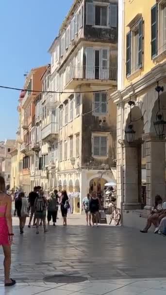科孚岛上的一条狭窄的街道高大的黄色建筑游客在城市里漫步 磁铁的销售生命在一座旅游城市的天空中如火如荼的高耸的建筑希腊 — 图库视频影像