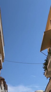 Korfu adasındaki dar sokaklar boyunca uzanan sarı binalar mıknatısların etrafında dolanıyor. Satış hayatı turistik bir şehirde, gökyüzünde yüksek binalarda, Yunanistan 09.09.2023