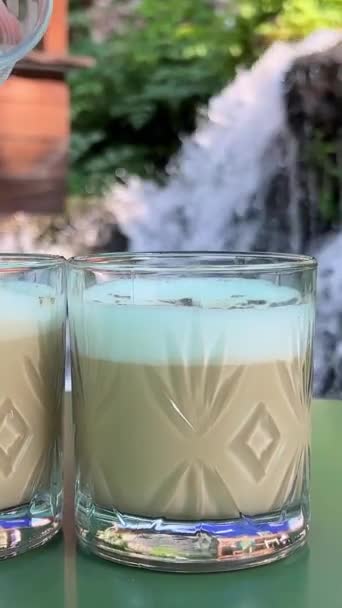 Tambahkan Batu Untuk Gelas Cappuccino Dengan Latar Belakang Air Terjun — Stok Video