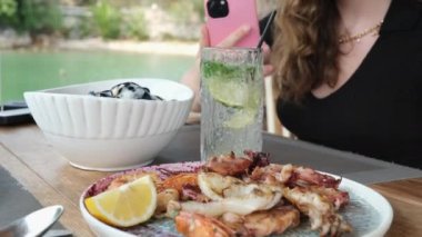 Kız cep telefonuyla deniz ürünleri tabağında tatlı ve ekşi soslu kremalı midye fotoğrafları çekiyor. Mojito. 