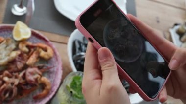 Kız cep telefonuyla deniz ürünleri tabağında tatlı ve ekşi soslu kremalı midye fotoğrafları çekiyor. Mojito. 