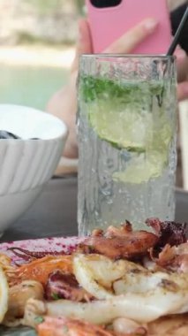 Kız cep telefonuyla deniz ürünleri tabağında tatlı ve ekşi soslu kremalı midye fotoğrafları çekiyor. Mojito. 