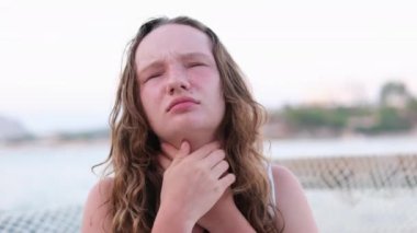 Yanmış ten kırmızı yanaklar ıslak saçlar. Sigorta şirketi, boğaz ağrısı çeken bir kızın yaz mevsiminde yüzme tatilinde soğuk algınlığına yakalanması önemlidir. Gölün arka planındaki kadın