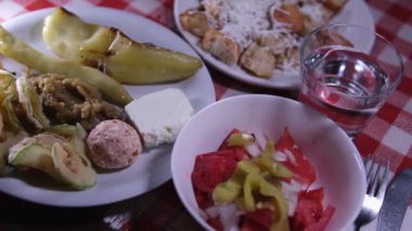 Makedonya 'daki bir restoranda, yemek kırmızı kare masa örtüsü üzerinde servis ediliyor. Izgara kabak, ızgara biber, domatesli salata peynirli çörek.