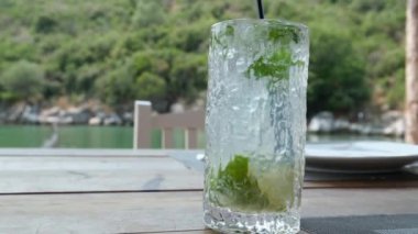 Barda ya da restoranda barmen tarafından hazırlanan mojito kokteyli sırasında şeffaf bardakta soda ve buz ile şeffaf bardağa düşen taze aromatik bitkinin süper yavaş çekim makrosu. 4k 