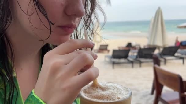 一个非常快乐的女孩在海滩上喝了一杯咖啡 露出她完美的手指好吧 她展示了穿着湿头发的绿色长袍放松生活的快乐 游完泳 — 图库视频影像