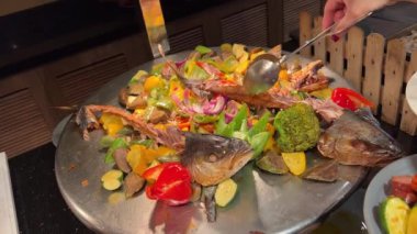 Suşi büfesinden lezzetli yiyeceklerle dolu beyaz bir tabak. Somon nigiri ve maki rulo. Bir el maki dürümlerinden birini yemek çubuğuyla alıyor. Suşi büfesi, Gıda Konsepti