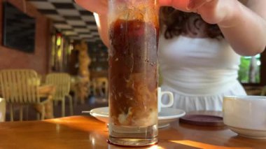 Kahverengi karbonatlı içecek bir kafede masanın üzerinde duruyor, el içeceğe pipet koyuyor, arka plan bokeh. Kokteyl. Yüksek kalite 