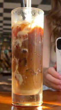 Bir kız cep telefonuyla bir fincan kahve videosu çekiyor. Bir bardak kahvenin fotoğrafını çekiyorum. Kadın eli, kafede akıllı telefonla kahve kokteylinin fotoğrafını çekiyor.