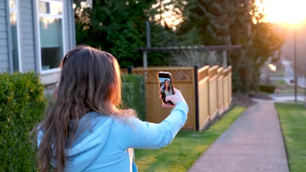 日落时 一位年轻女子在街上自作主张 她手里拿着一部手机站在房子旁边 — 图库视频影像