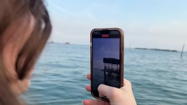女の子は携帯電話で水の上の家の写真を撮る — ストック動画