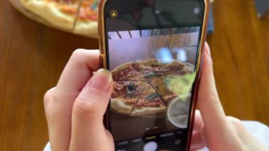 İtalyan pizzasının karton kutuda servis edilen akıllı telefon pizzasıyla fotoğrafını çeken bir kadın..