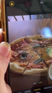 İtalyan pizzasının karton kutuda servis edilen akıllı telefon pizzasıyla fotoğrafını çeken bir kadın..