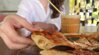 Beyaz arka planda pizza yiyen genç turist kadın. Fötr şapkalı, elinde pizza dilimiyle stüdyoda neşeli bir kadın..