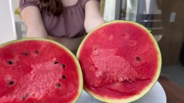 Genç bir kız elleriyle büyük bir karpuzu kırar.