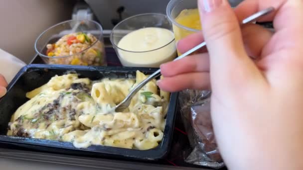 一名妇女的特写镜头是用飞机上的塑料容器里的肉吃意大利面 在商业飞机上吃饭的女人 人们在飞机上吃饭 乘客在飞行期间享用热饭 — 图库视频影像