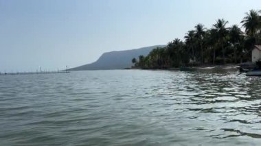Hareket halindeki bir teknenin gölün üzerine inşa edilmiş balık çiftliklerinin üzerinden manzarası. Çatısı olan, suyun üzerinde duran küçük bir ev. Arka plandaki yanardağa bakıyor. Kamera hareket ediyor..