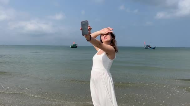 드레스에있는 소녀는 바다에서 셀카를 찍는다 — 비디오