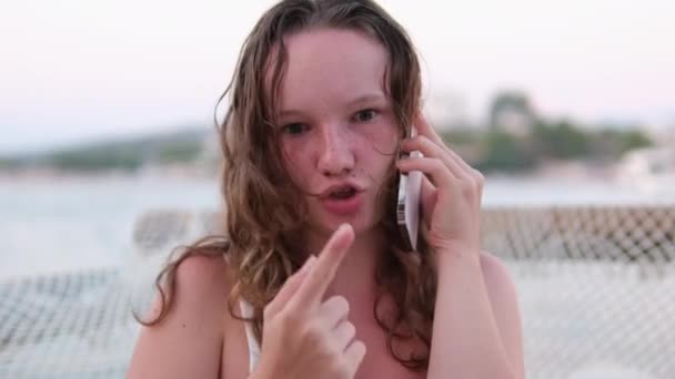 一个女人在电话上交谈 命令送货 与朋友交流 使用社交网络和互联网 在海滩上放松年轻女孩烧焦的皮肤 湿发的感情 — 图库视频影像