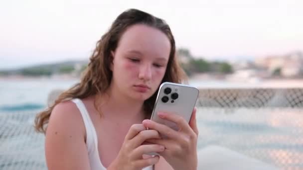 女の子は携帯電話をかぶり 配達を注文し 友人と通信し ソーシャルネットワークとインターネットを使用します 若い女の子のビーチの感情でリラックスして肌を燃やします 赤い頬のぬれた髪 — ストック動画