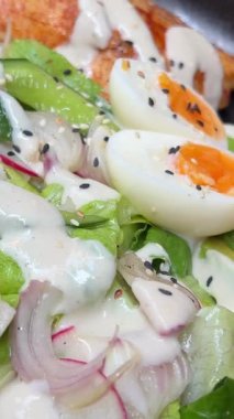 Marul yapraklı taze salata ve kaseye düşen domates. Beyaz masada sağlıklı besin maddeleriyle servis ediliyor. Ağır çekimde. Yumurta, avokado ve peynirli salata.