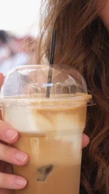 Güzel Avrupalı kız buzlu latte içiyor. Genç İspanyol kadın güneşli restoran terasında buzla bardağa kahve dolduruyor.