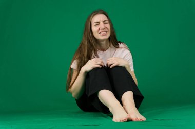 different emotions of a young girl on a green background chromakey beautiful facial features real people pink T-shirt white skinned. European. Young woman laughs very loudly studio photography clipart