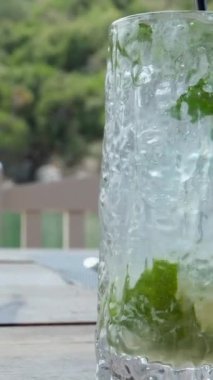 Barda ya da restoranda barmen tarafından hazırlanan mojito kokteyli sırasında şeffaf bardakta soda ve buz ile şeffaf bardağa düşen taze aromatik bitkinin süper yavaş çekim makrosu. 4k 
