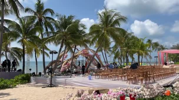 婚礼准备工作海滩上的婚礼装饰品 棕榈树海人们花婚礼装饰海滩设置海滨玫瑰拱门阳光明媚的夏天 — 图库视频影像