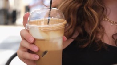 Güzel Avrupalı kız buzlu latte içiyor. Genç İspanyol kadın güneşli restoran terasında buzla bardağa kahve dolduruyor.