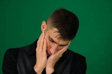 Yorgun adamlar. Yorgun genç adamların portresi, ellerini yüzlerinde tutarken. Yeşil arka plandaki yakışıklı bir adamın duyguları. Koyu renk, yakın plan, genç adam.