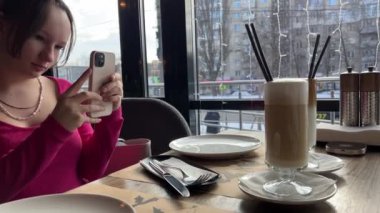 Kışın, bir kız fotoğraf çeker, içer, restoranda bir bardak buzlu latte içer, soğuk bir şeyler karıştırır.