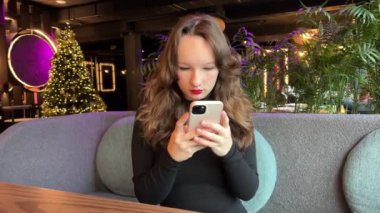 Kız telefon restoranı. Akıllı telefon kullanan bir kadın. Cep telefonu tutan pozitif İspanyol milenyum kızı. Gülümseyen Latince blog yazarı sosyal medyaya abone oluyor, internetten ürünler sipariş ediyor. satın al