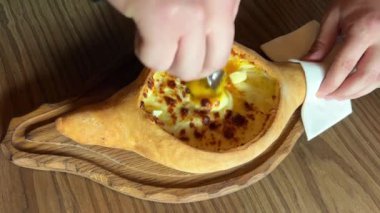 Tahta tahtada servis edilen yumurtalı Gürcü peynirli hamur işi khachapuri. Gürcistan Adjarian Khachapuri 'sinde suluguni peyniri ve yumurta sarısını karıştıran kişi.
