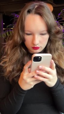 Kız telefon restoranı. Akıllı telefon kullanan bir kadın. Cep telefonu tutan pozitif İspanyol milenyum kızı. Gülümseyen Latince blog yazarı sosyal medyaya abone oluyor, internetten ürünler sipariş ediyor. satın al