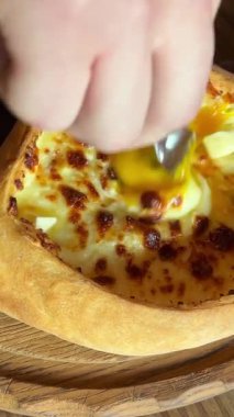 Tahta tahtada servis edilen yumurtalı Gürcü peynirli hamur işi khachapuri. Gürcistan Adjarian Khachapuri 'sinde suluguni peyniri ve yumurta sarısını karıştıran kişi.