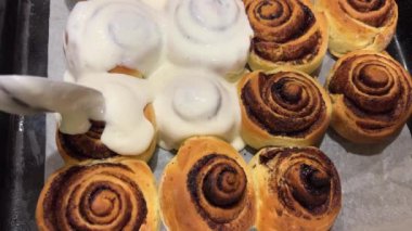 Taze pişmiş tarçınlı çöreklere ya da Cinnabon 'a krema dök. Tarçınlı ruloların üzerine tatlı krem peynirli krema dökülüyor. Tarçınlı çörek üretimi. Fırın ürünleri. İştah açıcı tarçın