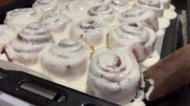 Taze pişmiş tarçınlı çöreklere ya da Cinnabon 'a krema dök. Tarçınlı ruloların üzerine tatlı krem peynirli krema dökülüyor. Tarçınlı çörek üretimi. Fırın ürünleri. İştah açıcı tarçın