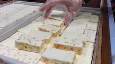 Kahverengi saçlı, örgülü, pembe tişörtlü iki kız dükkandan şeker seçip alıyor. Pastila dükkanda.