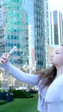 Büyük bir şehirde bir gökdelenin arka planında, mor elbiseli genç bir kız, elindeki akıllı telefonun aynasına bakar ve seyahat etmeyi sever.