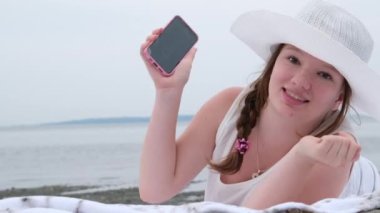 Joy surprise girl laughs Girl on beach with mobile phone, white hat lying on masons watching Pretty Blond Woman Laying Down