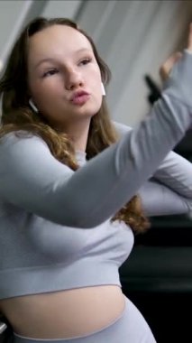 Sporty girl in blue top taking selfie on phone. Girl takes a selfie in the GYM