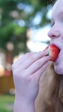 happy girl eating strawberries in summer in garden. Delicious strawberry dessert. Red-haired girl eats strawberries in nature