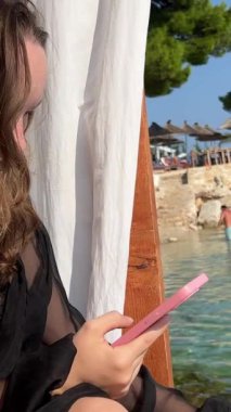 İnternet kablosuz ağı iyi sosyal ağlar. Genç bir kız deniz kenarındaki perdelerle VIP salonunda oturuyor. Arnavutluk 'un arka planında çam ağaçları ve dağlar yüzüyor. kayalar