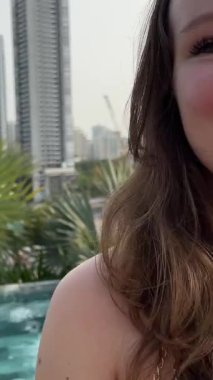 A very satisfied happy girl near the pool received good news on the phone, laughs, rejoices, smile of happiness. A young woman shows her phone, talks about the news, joy, laughter
