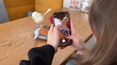 Bir kız blogger düz bir kruvasanın videosunu çekiyor, sonra onu ısırıyor, arka planda duran iki porsiyon dondurmayı tadıyor, kiraz ve vanilya. Tatlı lezzetli.